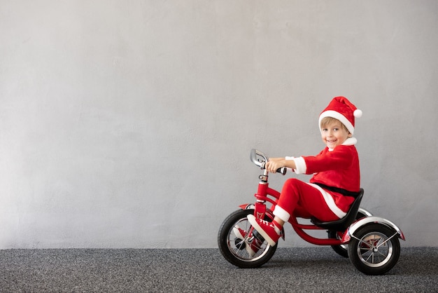 Gelukkig kind dat kerstkostuum draagt Kid rijdt op de fiets Grappig kind aan het spelen