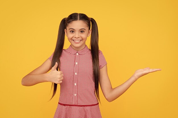 Gelukkig kind dat product presenteert op gele achtergrondkopieerruimte toont duim omhoog reclame