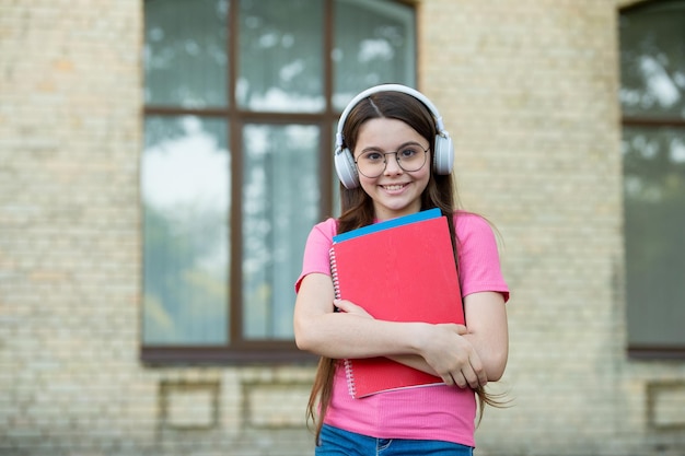 Gelukkig kind draagt een moderne koptelefoon met schoolboeken buiten audiocursus