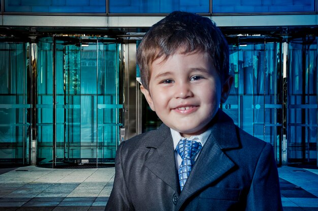Gelukkig kind gekleed zakenman met handen in zijn stropdas en wolkenkrabbers op de achtergrond