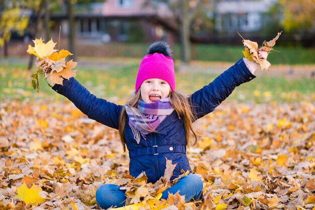 Gelukkig kind gooien herfstbladeren en glimlachen buitenshuis.