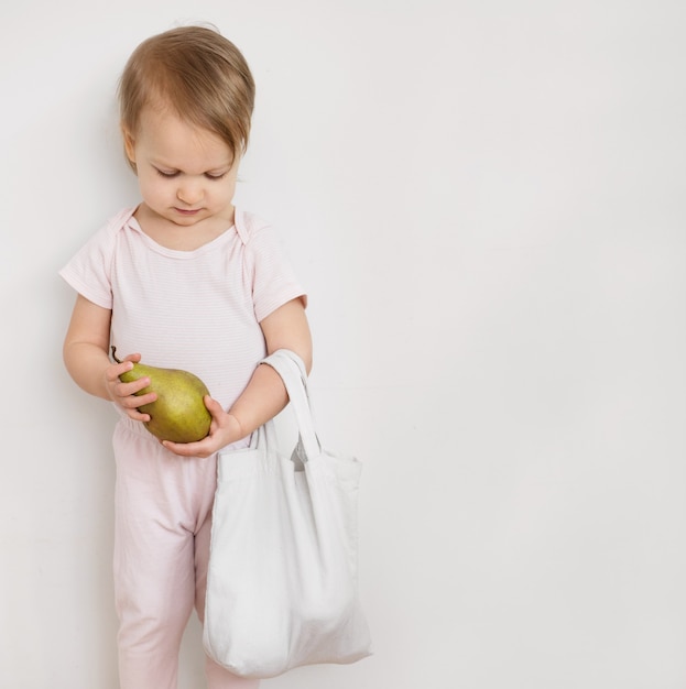 Gelukkig kind houdt perenfruit vast uit eco herbruikbare stoffen tas