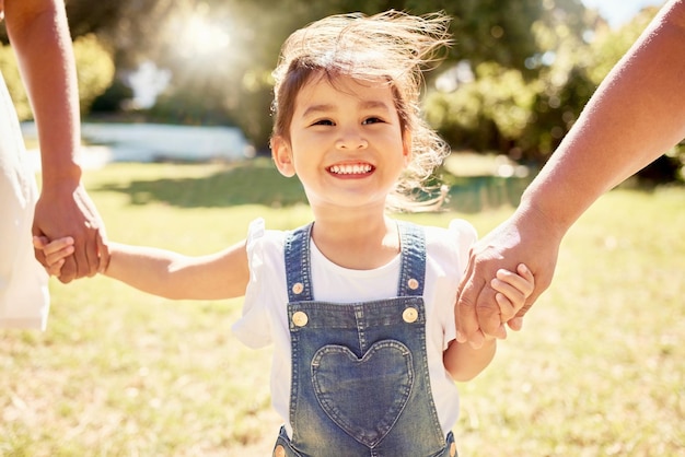 Gelukkig kind in de zon en wandelen met de ouders in het natuurpark met een glimlach die de handen van het meisje vasthoudt in de zomerzon kind in de tuin glimlachend op gras en familie ontspannen genieten van weekend kindertijd buiten vrijheid