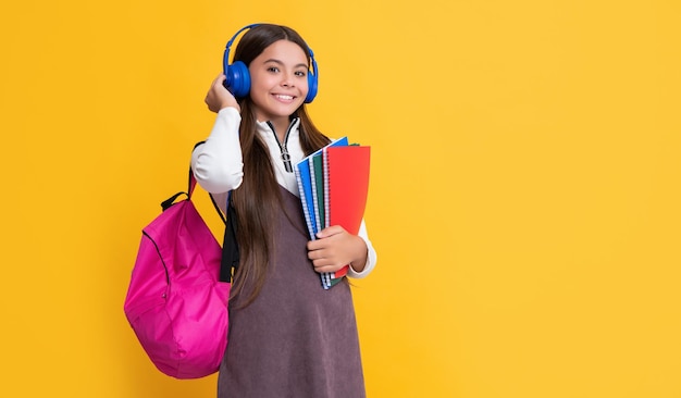 Gelukkig kind in koptelefoon met schoolrugzak met werkmap op gele achtergrond