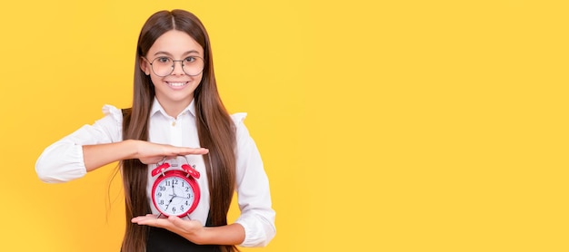 Gelukkig kind in schooluniform en bril met wekker die tijd schooltijd toont tiener kind met klok alarm horizontale poster banner koptekst kopie ruimte