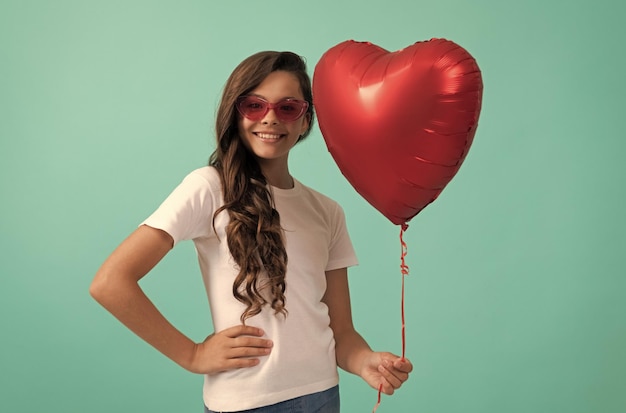 Gelukkig kind in zonnebril houdt rode hartfeestballon vast voor Valentijnsdag liefdessymbool liefde