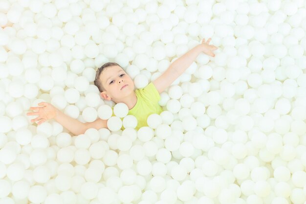 Gelukkig kind jongen in het grote droge zwembad met duizenden witte ballen Jeugdconcept Indoor vrijetijdsbesteding Plezier in de speelkamer