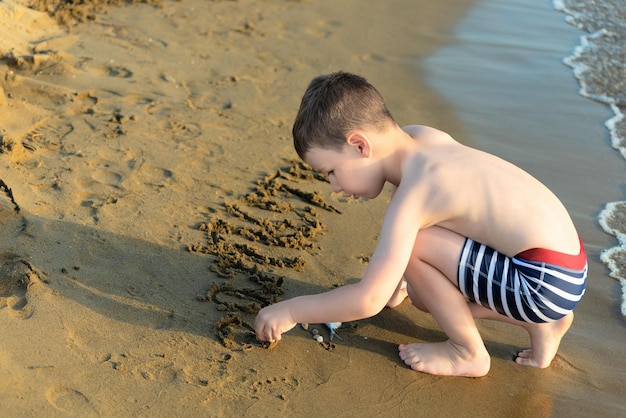 Gelukkig kind jongen spelen met zand aan de kust Zomer en reizen concept