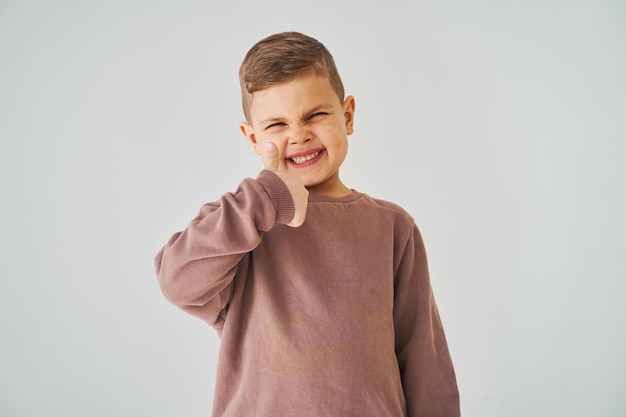 Gelukkig kind jongen toont duimen omhoog en glimlacht op witte achtergrond Knappe jongen poseren en glimlachen