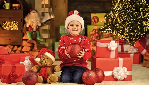 Gelukkig kind kerstmuts zoon klaar om wintervakantie te vieren kleine jongen opgewonden met aanwezig kind houdt decoratief balbeer speelgoed cadeau voor kerst vrolijk kerstfeest gelukkig nieuwjaar