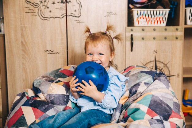 Gelukkig kind, klein meisje dat met een bal speelt terwijl ze in een zachte stoel zit. kind speelt met een bal.