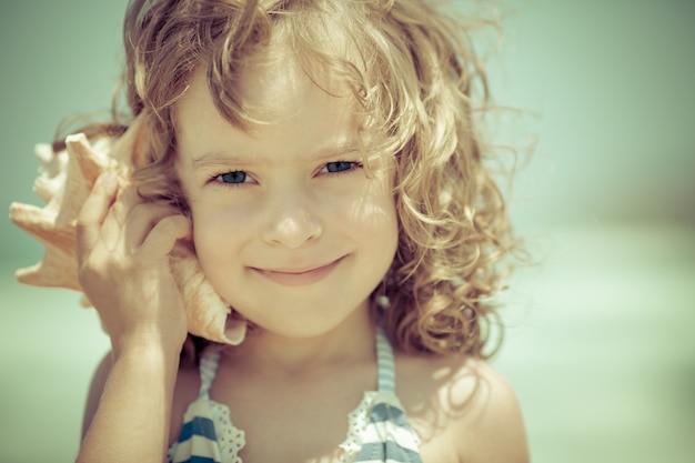 Foto gelukkig kind luistert naar zeeschelp op het strand zomervakanties concept