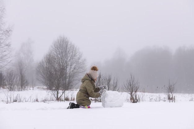 Gelukkig kind maakt een sneeuwpop in een besneeuwd veld op het platteland.