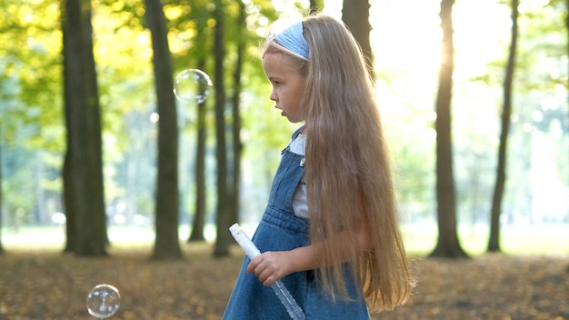 Foto gelukkig kind meisje blaast zeepbellen buiten in zomer park.