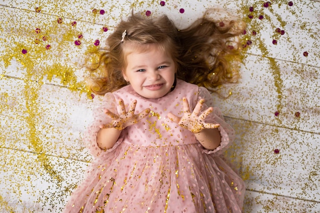 Gelukkig kind meisje in roze jurk liggend op de vloer met confetti en haar verjaardag vieren