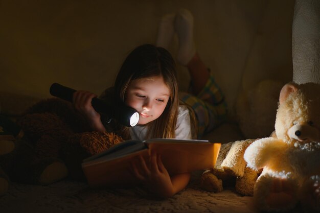 Gelukkig kind meisje lacht en leest boek in het donker in een tent thuis