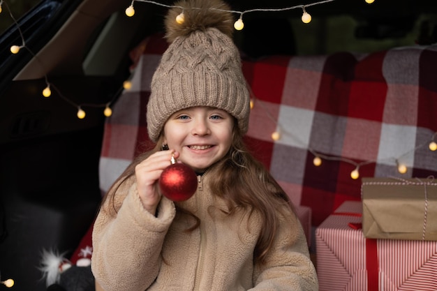 gelukkig kind meisje met plezier in versierde kofferbak van een auto met kerstcadeaus