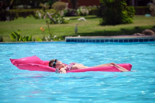 Gelukkig kind meisje ontspannen op opblaasbare luchtbed in zwembad op zonnige zomerdag tijdens tropische vakanties Zomeractiviteiten concept