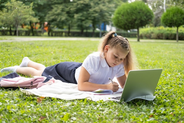 gelukkig kind meisje op schooluniform met notebook heeft online les op laptop op gazon