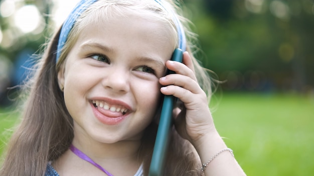 Gelukkig kind meisje praten op mobiele telefoon in zomer park.