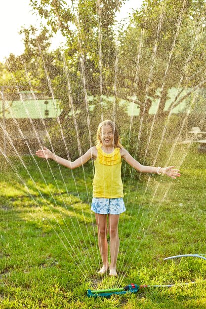 Gelukkig kind meisje spelen met tuin sprinkler rennen en springen zomer