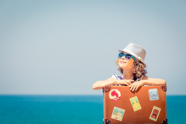 Gelukkig kind met koffer op het strand Kind geniet van een zomervakantie aan zee Reis- en vakantieconcept