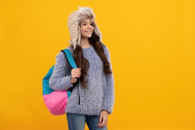 Gelukkig kind met krullend haar in hoed. terug naar school. tienermeisje in breigoed op gele achtergrond.