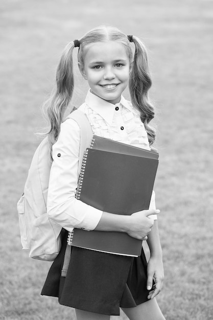Gelukkig kind met lange haarstaarten in schooluniform houdt studieboeken buiten kennis vast