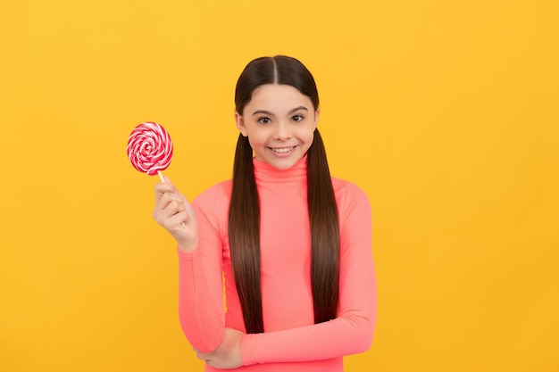 Gelukkig kind met lolly snoep op stok op gele achtergrond zoet leven