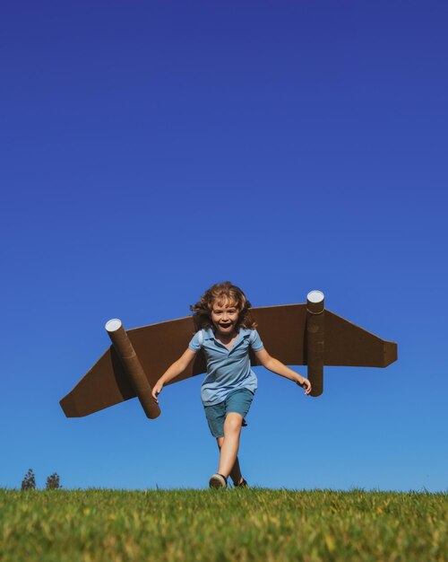 Gelukkig kind met papieren vleugels tegen blauwe lucht Kind met speelgoedjetpack plezier in lente groen veld