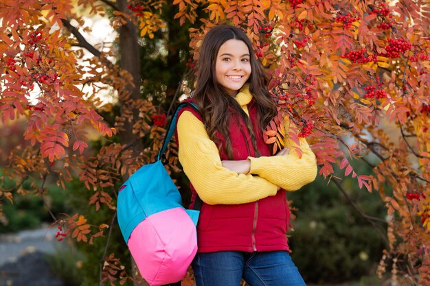 Gelukkig kind met schooltas in de buurt van kleurrijke herfstbladeren op rowanberry tree september