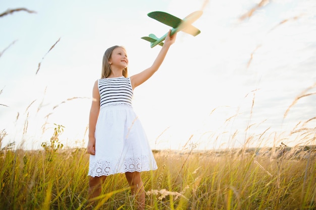 Foto gelukkig kind met speelgoedvliegtuig speelt bij zonsondergang