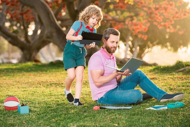 Gelukkig kind met vader die buiten leert door online te studeren en op laptop te werken