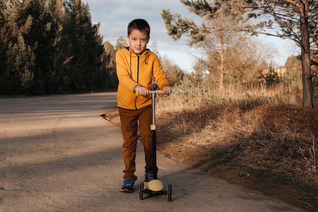 Gelukkig kind op een scooter in het park. Kinderen leren rijden op rolplanken. Actieve recreatie voor kinderen in een veilige woonstraat. Actieve sporten voor kleuters.