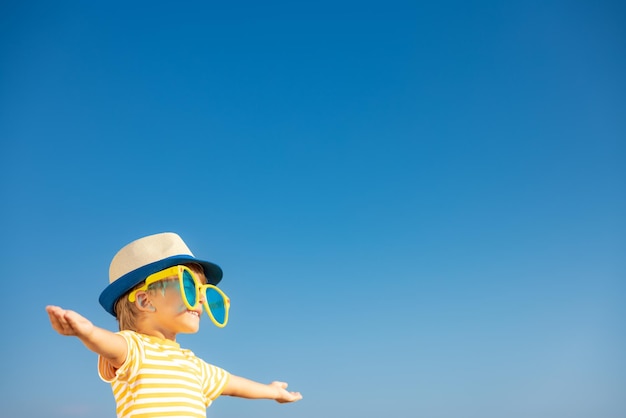 Gelukkig kind plezier buiten tegen blauwe hemelachtergrond. Portret van lachende jongen op zomervakantie. Vrijheid en reisconcept