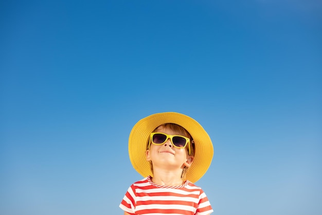 Gelukkig kind plezier buiten tegen blauwe hemelachtergrond. Portret van lachende jongen op zomervakantie. Vrijheid en reisconcept