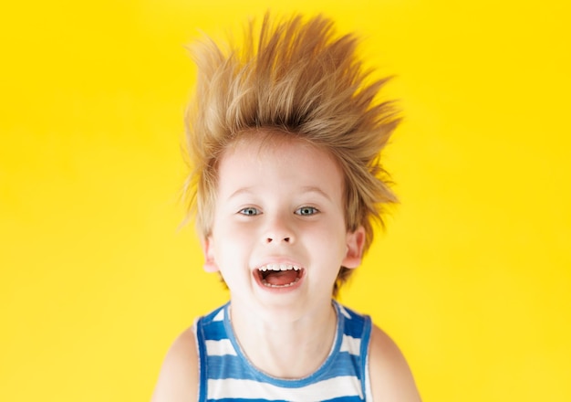 Gelukkig kind schreeuwt tegen de achtergrond van geel papier Grappig kind dat ondersteboven hangt Zomervakantie en reisconcept