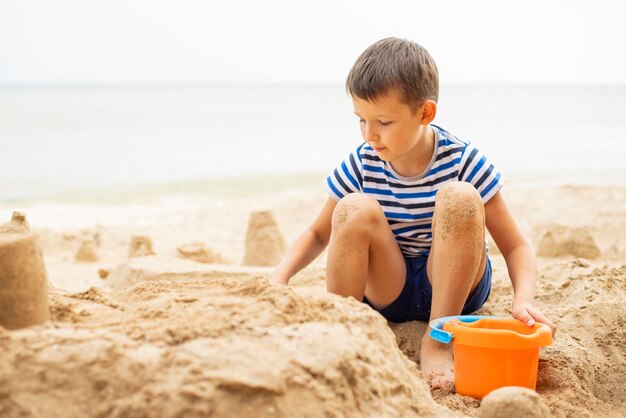 Gelukkig kind speelt met zand op het strand in de zomer Jongen bouwt een zandkasteel op de zee