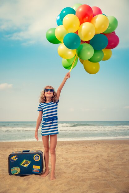 gelukkig kind spelen met kleurrijke ballonnen en met een koffer op het strand