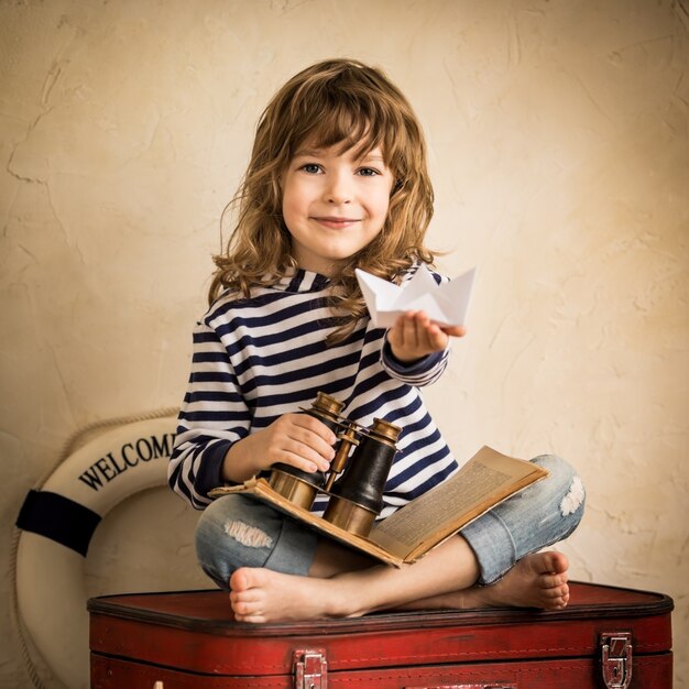 Gelukkig kind spelen met papieren zeilboot binnenshuis. Reis- en avontuurconcept