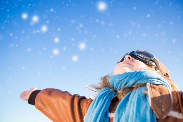 Gelukkig kind spelen met speelgoed vliegtuig tegen blauwe winter hemelachtergrond