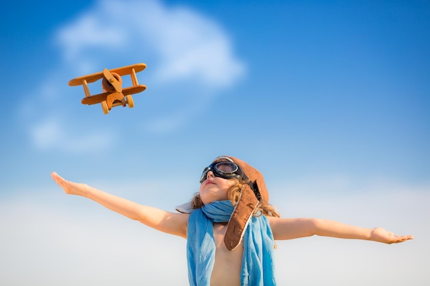 Gelukkig kind spelen met speelgoed vliegtuig tegen blauwe zomer hemelachtergrond