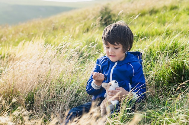 Gelukkig kind spelen met stro gras zittend op de weide in de heuvel, kind jongen zittend op het gras op de boerderij veld buiten spelen met zijn speelgoed