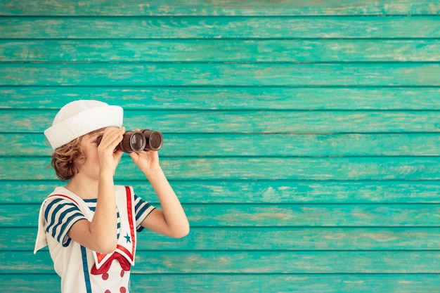 gelukkig kind zit met een verrekijker gekleed als een zeeman op blauwe houten achtergrond