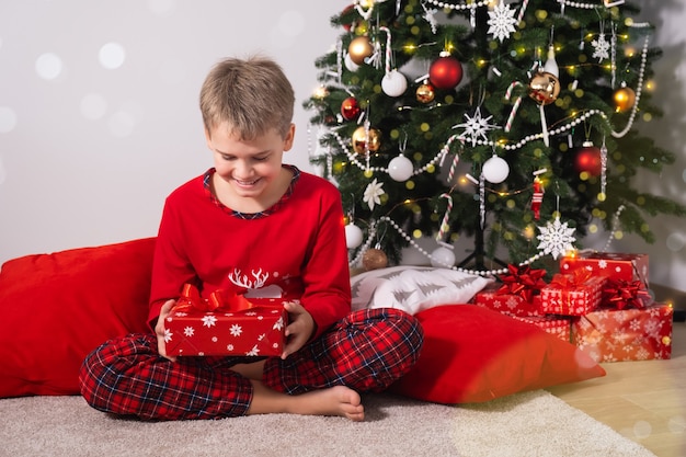 Gelukkig kind zit thuis op de vloer en houdt een kerstcadeau bij de kerstboom