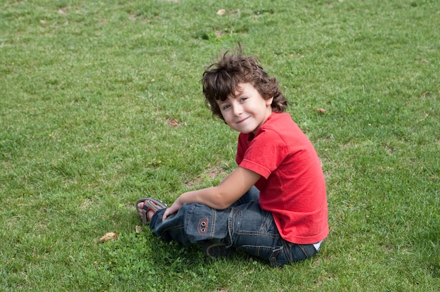 Gelukkig kind zittend op het gras met rood shirt