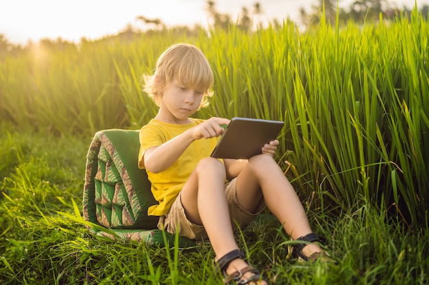 Gelukkig kind zittend op het veld met tablet Jongen zittend op het gras op zonnige dag Thuisonderwijs of een tablet spelen