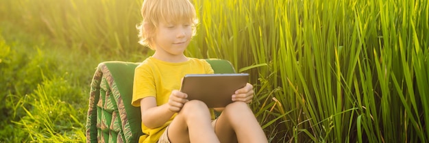 Gelukkig kind zittend op het veld met tablet jongen zittend op het gras op zonnige dag thuisonderwijs