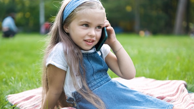 Gelukkig kindmeisje dat op mobiele telefoon in de zomerpark spreekt