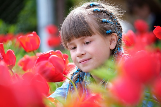 Gelukkig kindmeisje dat van zoete geur van rode tulpenbloemen in de zomertuin geniet